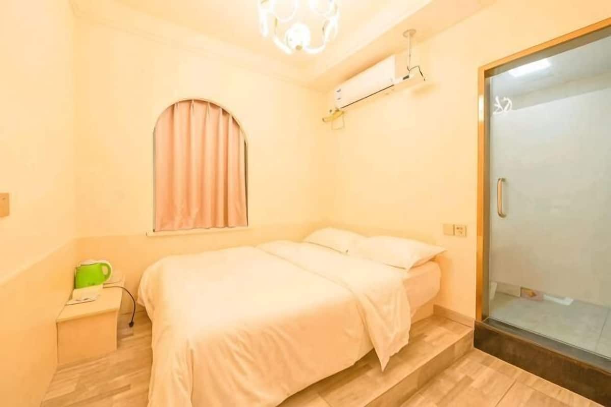 Ein Schlafzimmer mit zwei Betten, einem Fenster mit Vorhängen, einem Nachttisch mit einem grünen Gegenstand und einer Schiebetür zum Badezimmer.