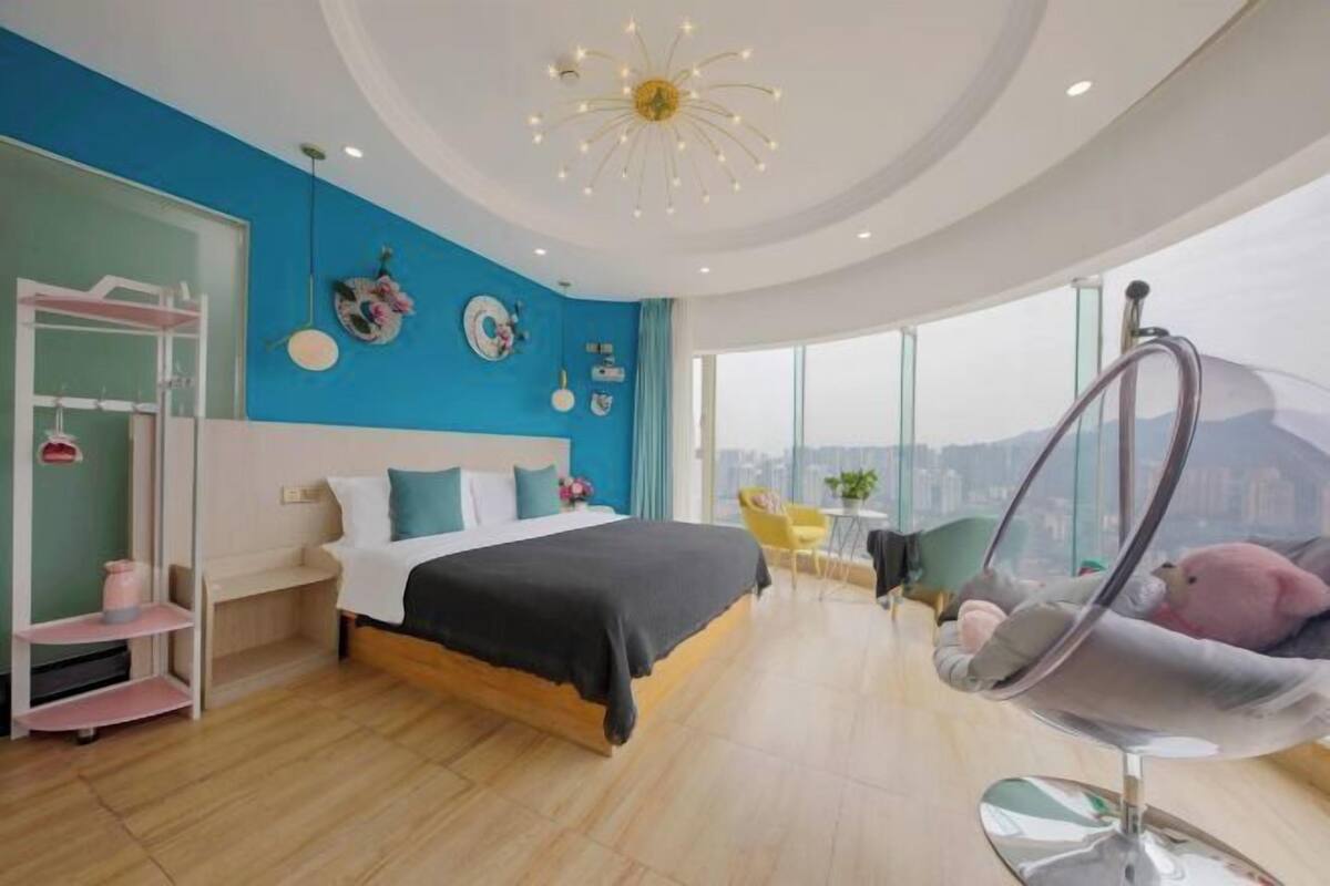 Ein modernes Schlafzimmer mit einem großen Bett, einem Hängekorbsessel und Blick auf die Stadt.