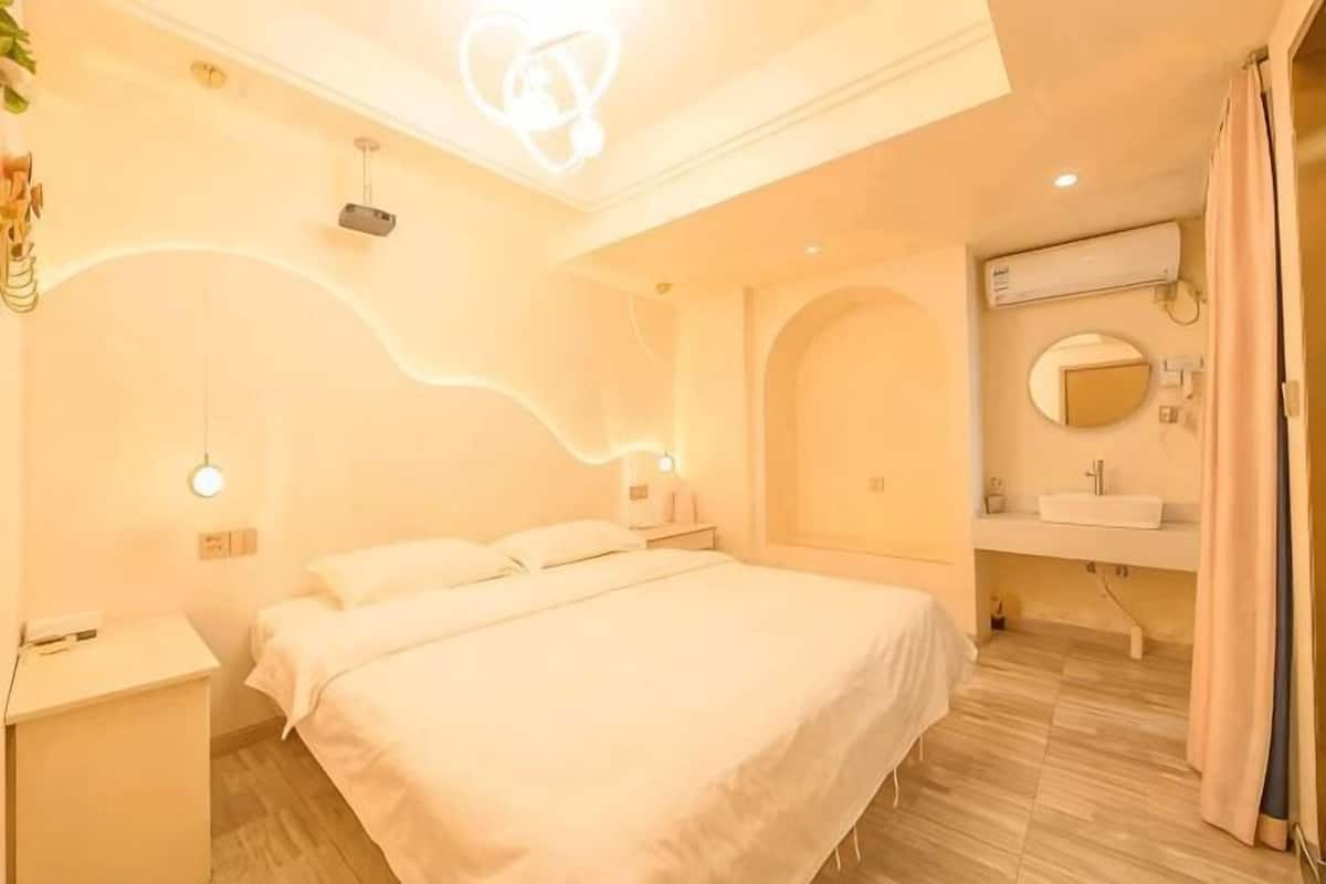 Ein Hotelzimmer mit Bett, Nachttisch, Wandleuchte und einem Badezimmer mit Waschbecken und Spiegel.
