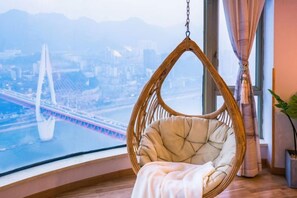 A hanging chair with a cushion, a large window with a view of a bridge and cityscape, and a potted plant. - Meitu Apartment Hotel (Chongqing Jiefangbei Chaotianmen Branch) (Chongqing)