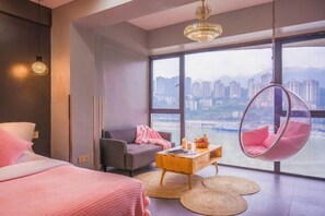 Habitació d'hotel moderna amb una finestra gran, una cadira penjant, un sofà i un llit.