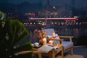 Un balcón con vistas a un paisaje urbano nocturno, con una mesa, una silla, velas y un libro.
