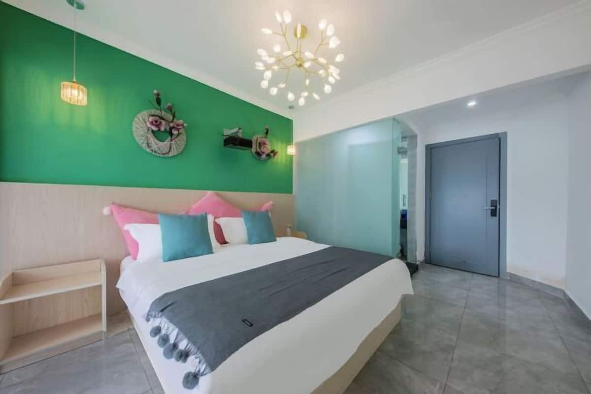 Ein Schlafzimmer mit Bett, grüner Wand, einer Chandeliebre und einer Tür.