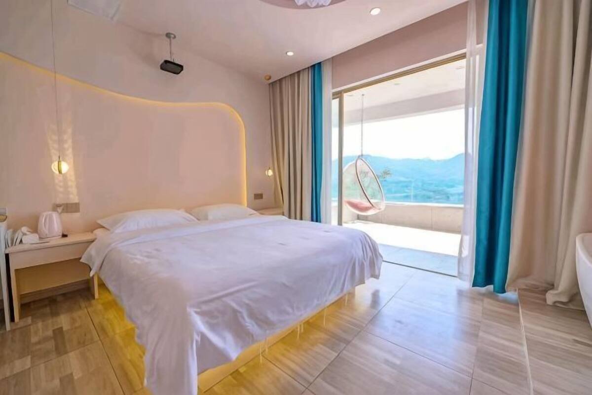 Ein Hotelzimmer mit einem Bett, einem Nachttisch, einem Sessel und Blick ins Freie.