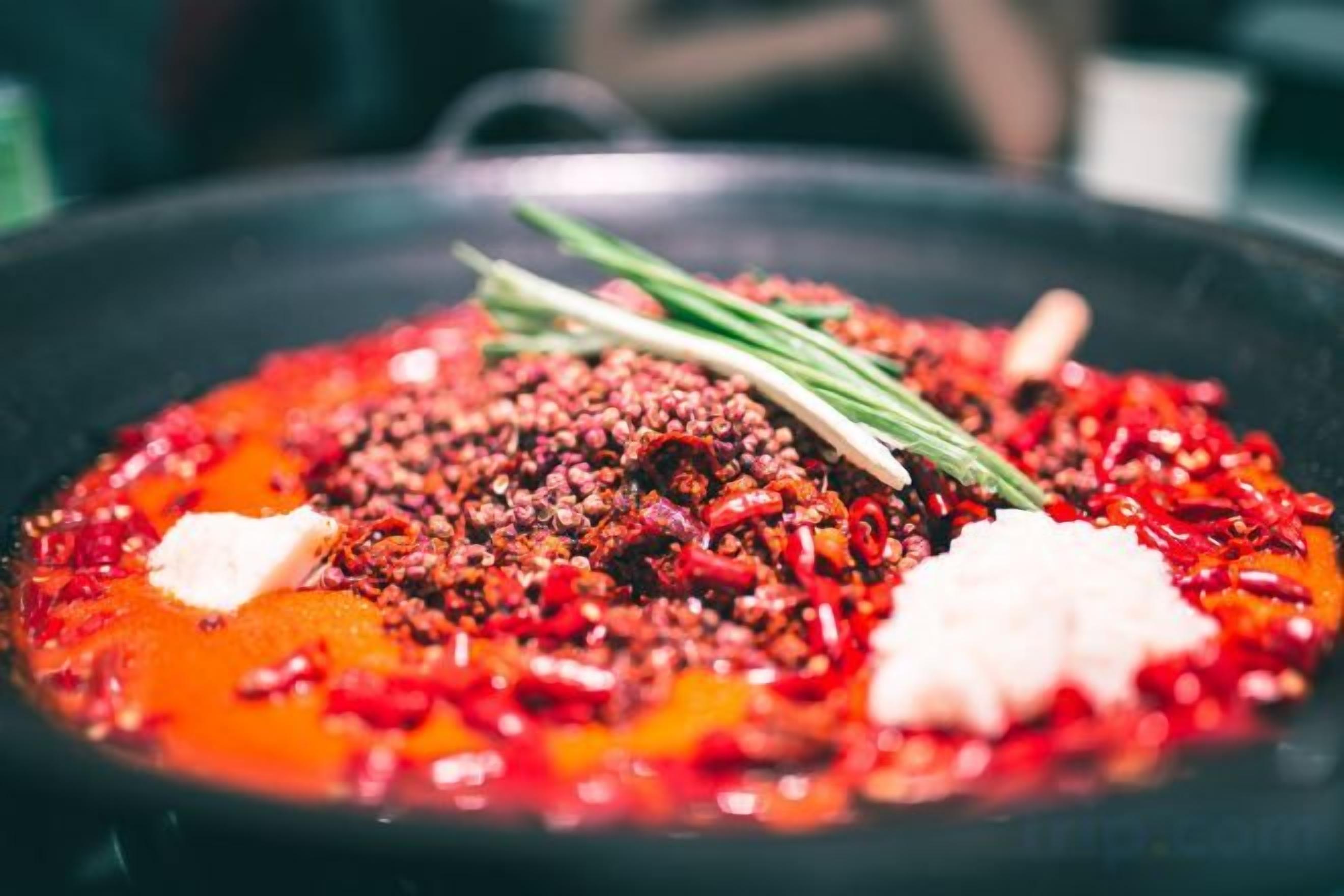 A close-up of a dish with red chili flakes, a dollop of white cream, and green herbs on a black plate.
