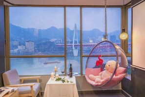Una habitación con un ventanal grande, un sillón colgante, una mesa con una botella y una silla.