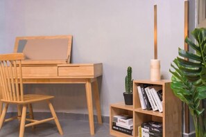 Un escritorio de madera con una silla, una estantería con libros y una pequeña planta en maceta, y un jarrón alto.