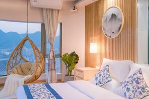Un dormitorio con una silla colgante, una cama con almohadas estampadas, una mesita de noche con lámpara y vistas a la ciudad.