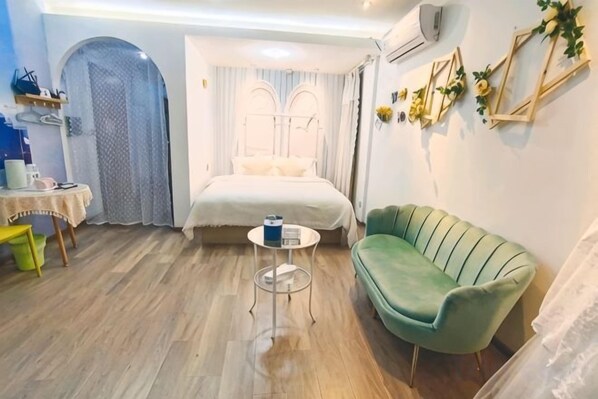 Una habitación con una cama, un sofá verde, una mesita redonda y una puerta que da a otra estancia.