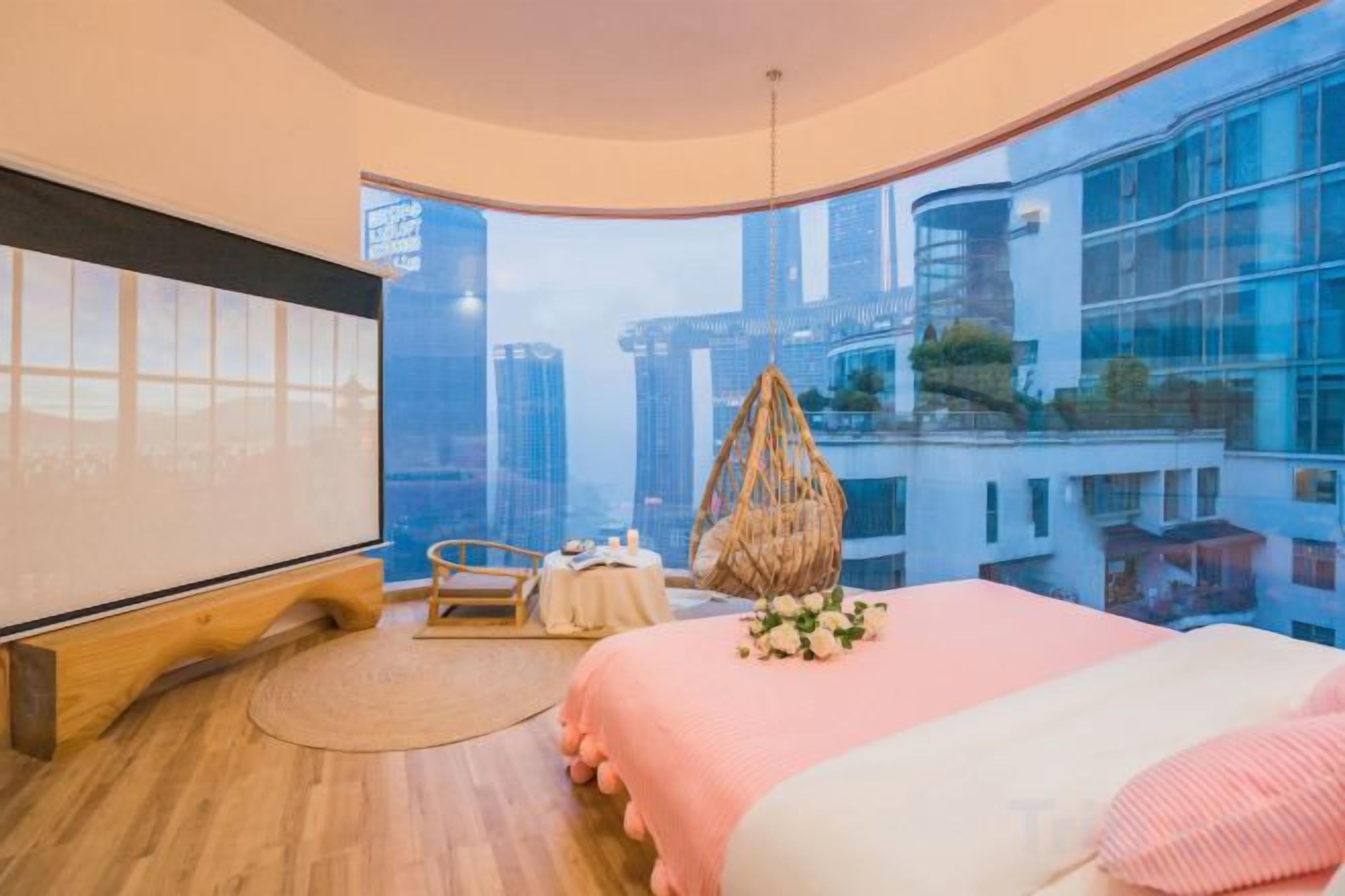 Une chambre moderne avec un grand lit, un fauteuil suspendu et une vue sur le paysage urbain.