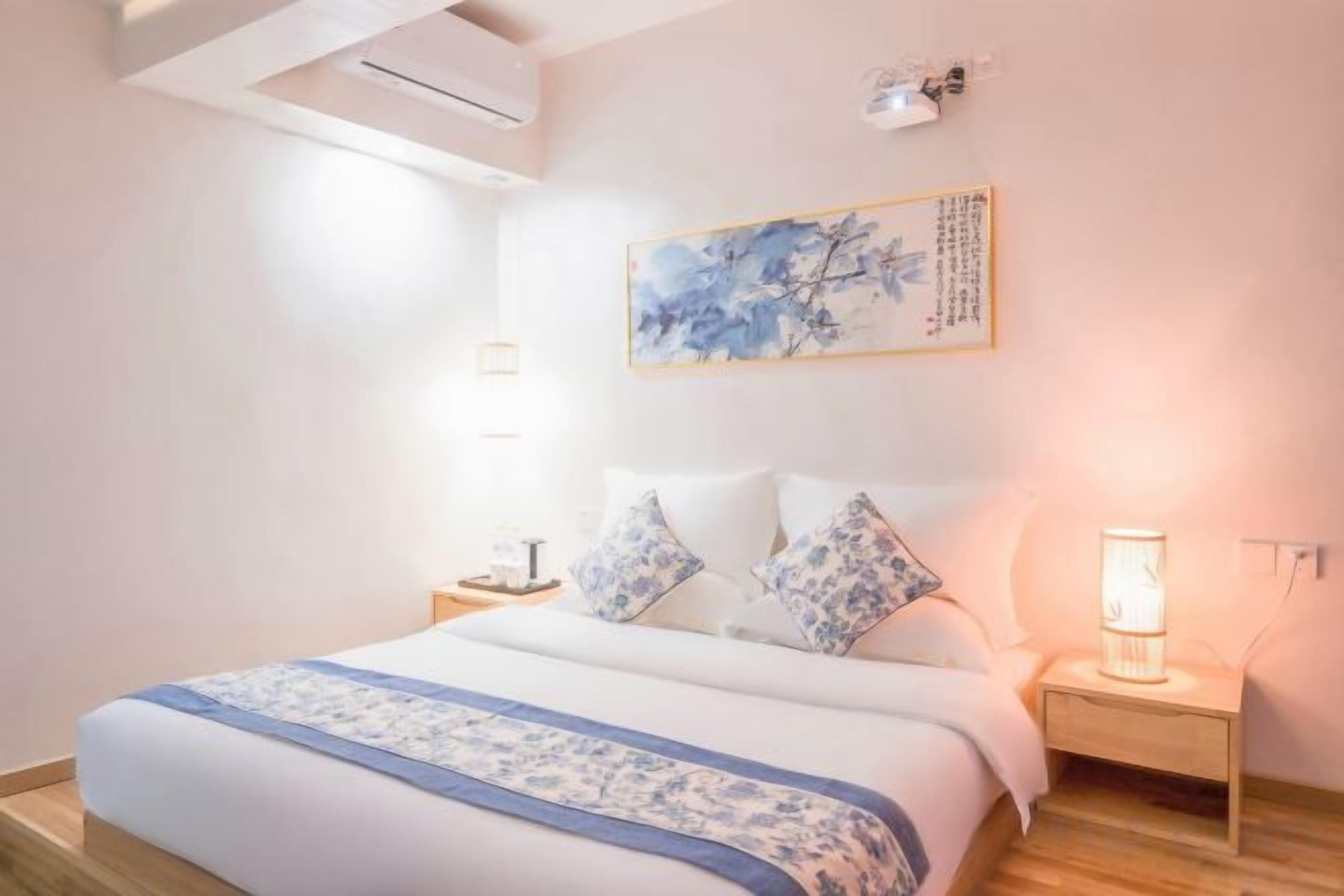 Una habitación de hotel con cama, lámparas de noche, una obra de arte en la pared y un ventilador de techo.