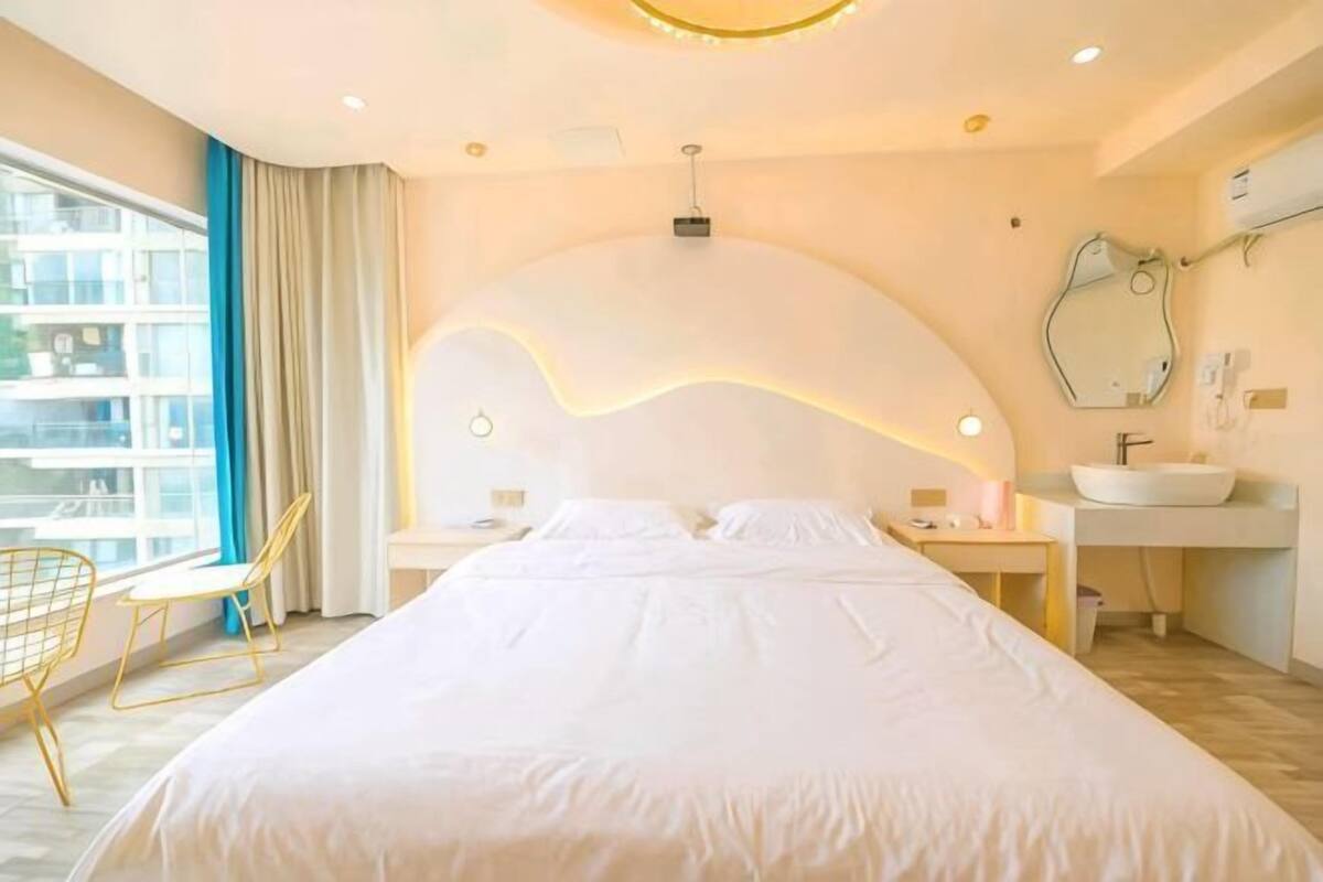 Ein Hotelzimmer mit einem großen Bett, einem Nachttisch, einem Sessel, einem Fenster mit Blick und einem Badezimmer mit Waschbecken und Spiegel.