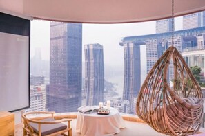 A room with a view of tall buildings, a hanging chair, a table with a book and candle, and a wooden chair. - Meitu Apartment Hotel (Chongqing Jiefangbei Chaotianmen Branch) (Chongqing)