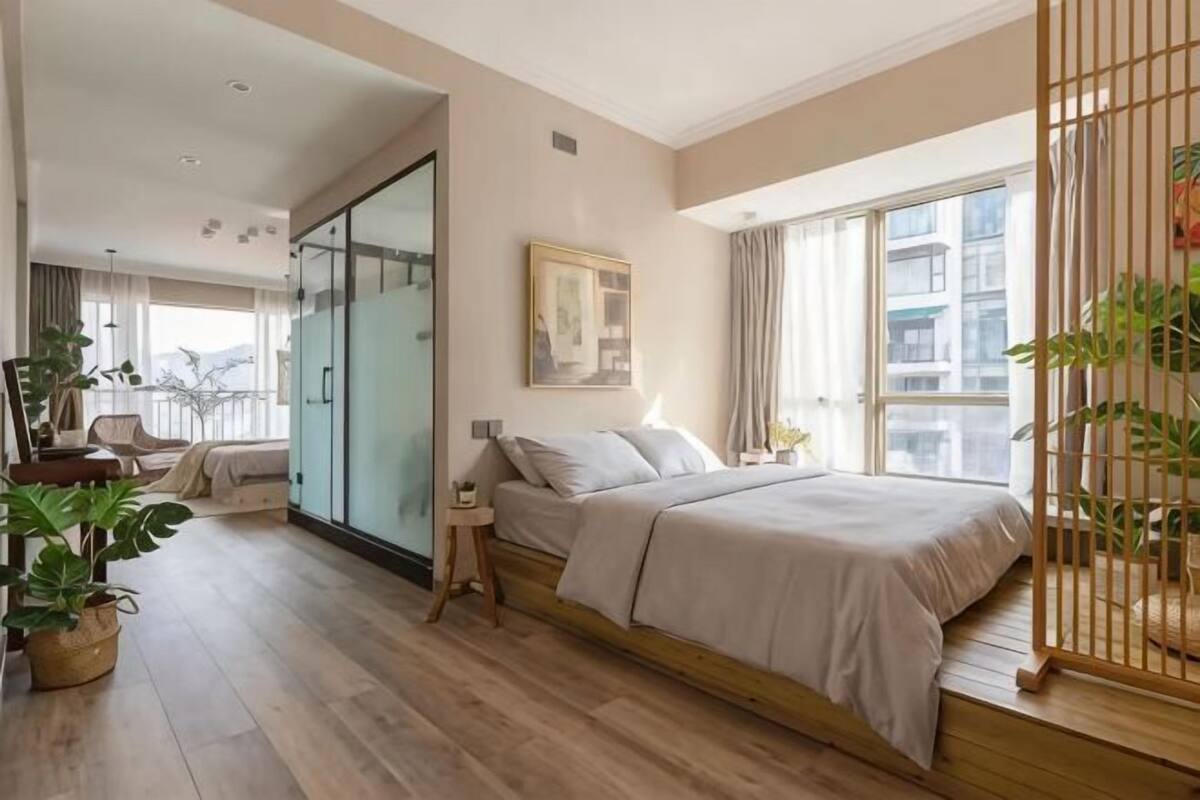 Ein modernes Schlafzimmer mit einem großen Bett, einer Glastür, die auf einen Balkon führt, und Blick auf Gebäude.