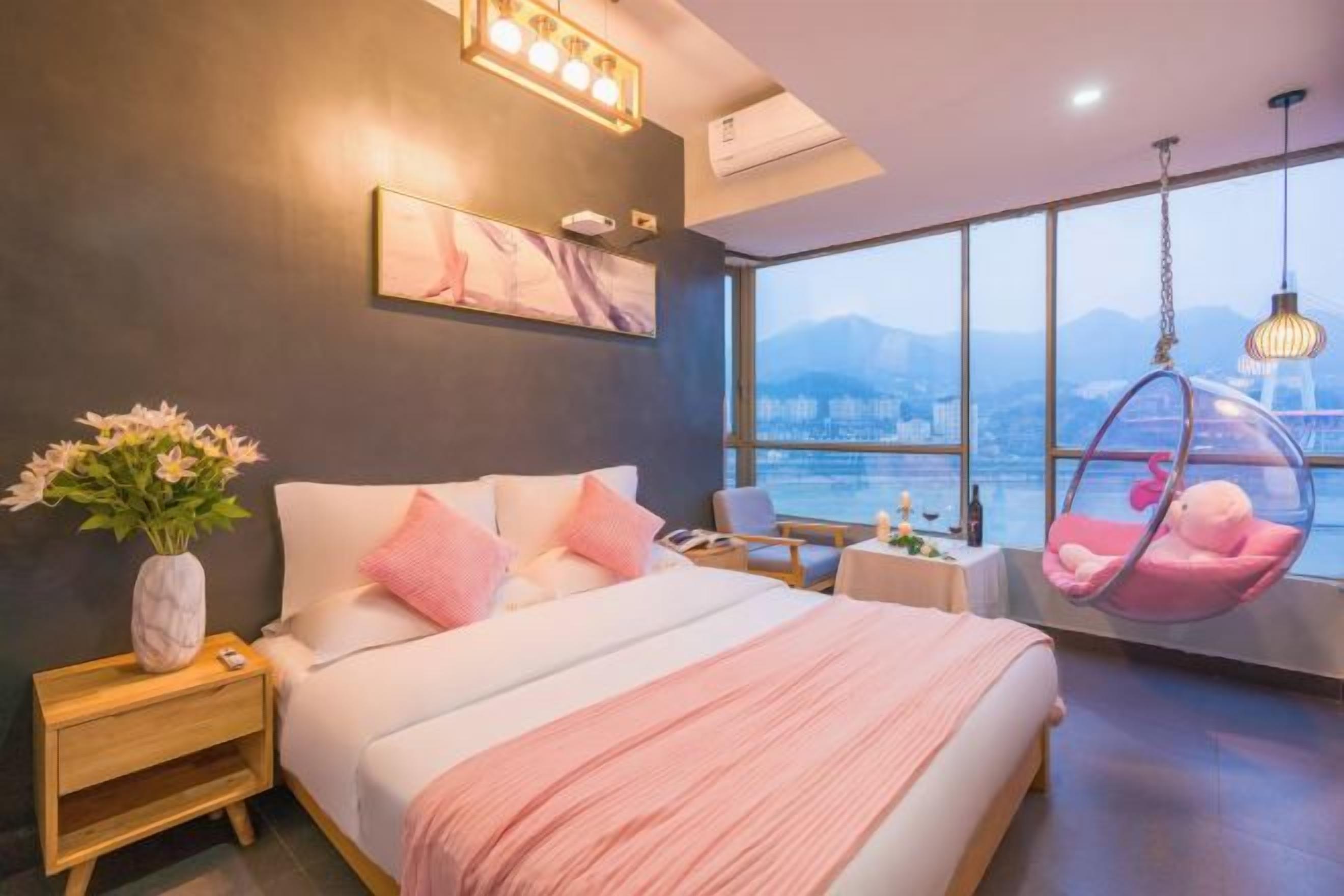 A modern bedroom with a large bed, bedside tables, a hanging chair, and a view of the city.