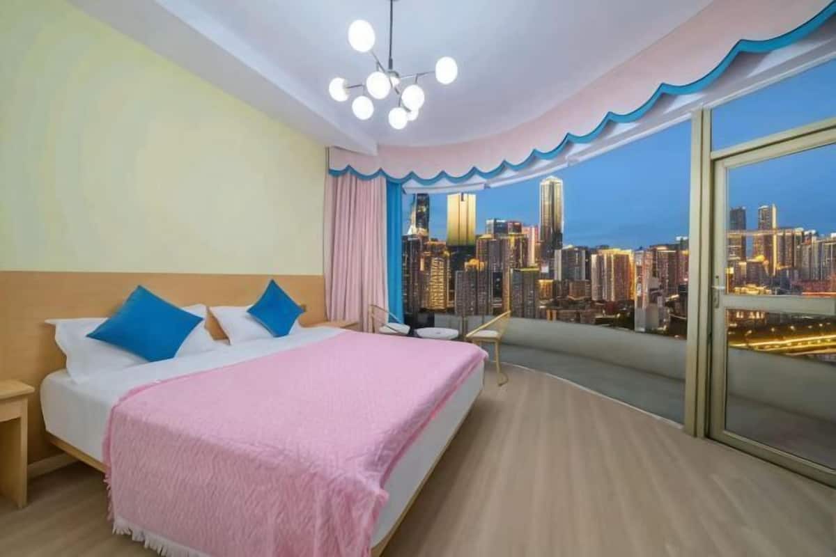 Ein Schlafzimmer mit Blick auf die Stadt, ein Bett mit Kissen, ein Nachttisch und ein Sessel.