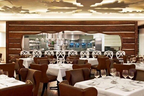 A restaurant with multiple tables, each set with white tablecloths and brown chairs.