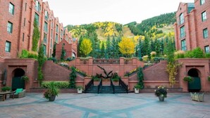 A courtyard with a central staircase, brick buildings, and a hillside with trees.