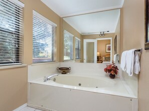 Ein Badezimmer mit einer großen Badewanne, einem Waschtisch mit Spiegel und einem Fenster mit Jalousien.