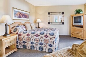 Ein Hotelzimmer mit einem Bett, einem Nachttisch mit einer Lampe, einem Schrank mit einem Fernseher und einem Spiegel an der Wand.