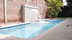 A rectangular swimming pool with a water feature, surrounded by a brick wall and potted plants. - Hotel Boutique Nueva Valladolid (Comayagua)