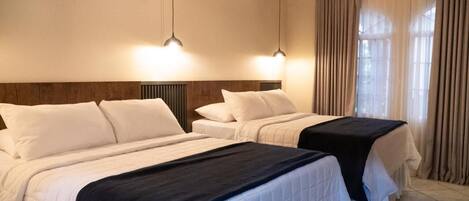 A hotel room with two beds, a wooden headboard, a window with curtains, and pendant lighting.