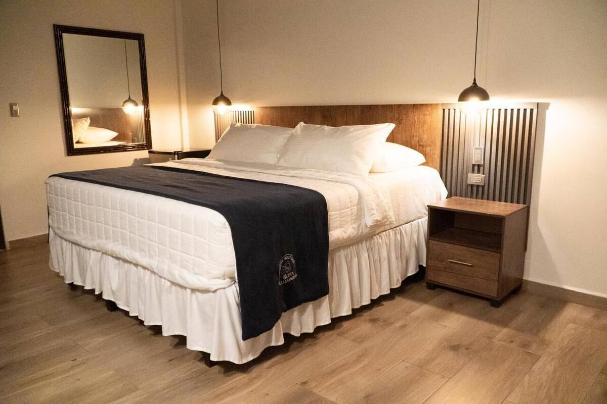 A neatly made bed with a wooden headboard, a bedside table, and a wall-mounted mirror.