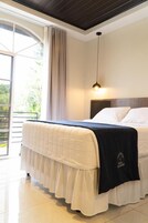 Habitación de hotel con cama, ventana con cortinas, lámpara de techo y vistas a zonas verdes.