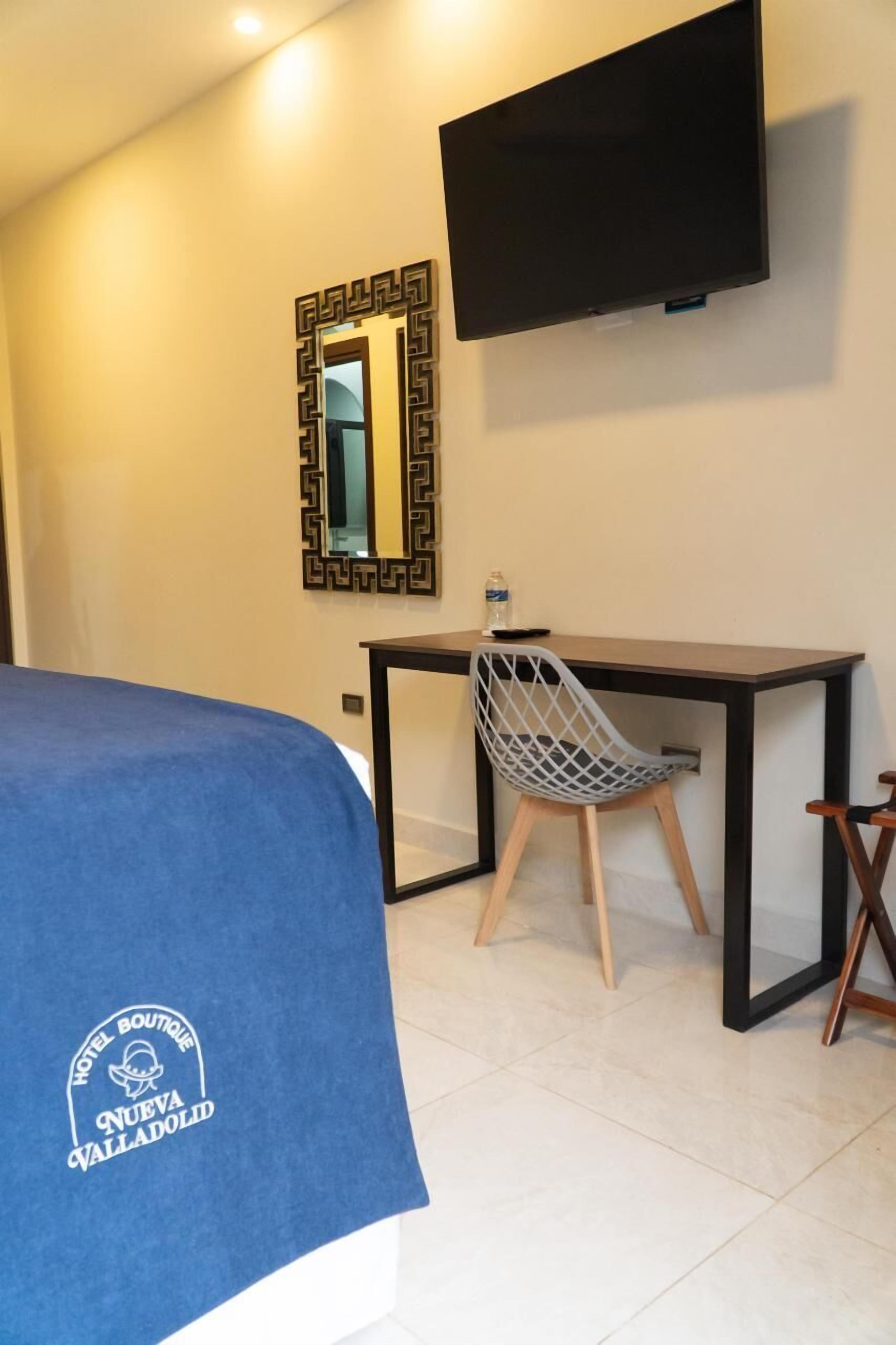 A hotel room with a bed, a desk, a chair, a TV, and a mirror.