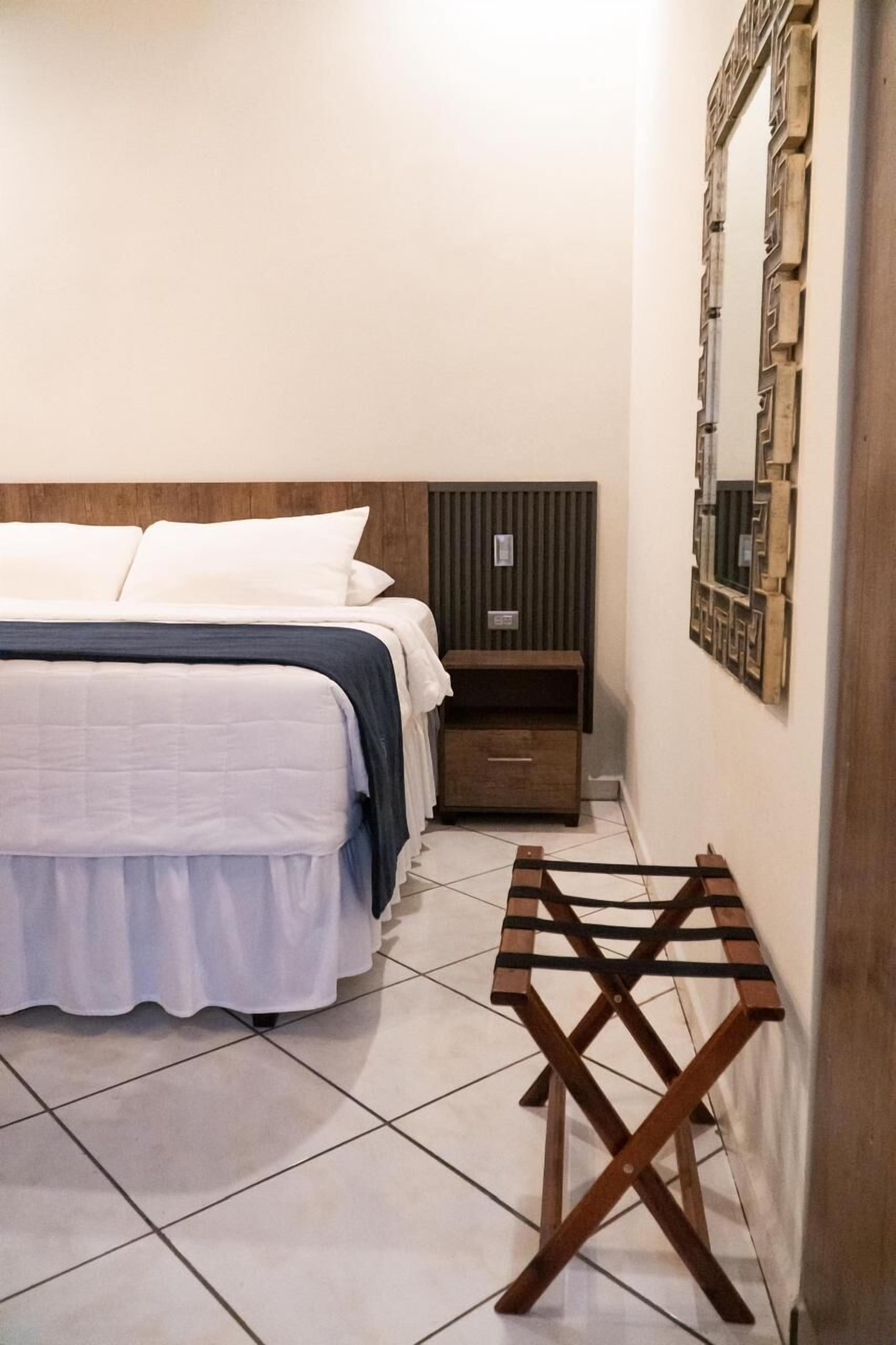 A neatly arranged bedroom with a bed, bedside table, and a small wooden stool.