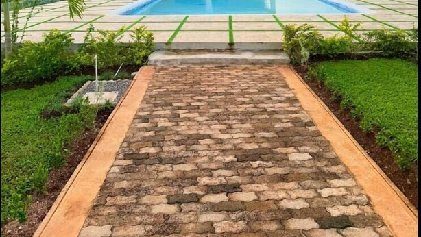 Una casa moderna con piscina, un camino de ladrillo que lleva a la piscina y vistas del paisaje circundante.
