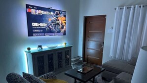 Una sala de estar con una televisión de pantalla plana mostrando un juego, sofás con diseño, una mesa de centro y un aparador.