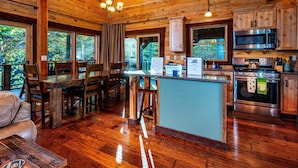 A wooden cabin interior with a dining area, kitchen, and large windows. - 3 Irish Sons, 4BR, 3 BA  Log Cabin in the woods. (Nashville)