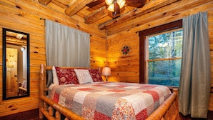 A log cabin bedroom with a wooden bed, a large window, and a mirror on the wall. - 3 Irish Sons, 4BR, 3 BA  Log Cabin in the woods. (Nashville)