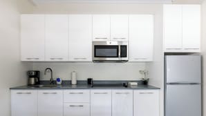 Eine moderne Küche mit weißen Schränken, einer eingebauten Mikrowelle, einem Edelstahlkühlschrank und einer Kaffeemaschine auf der Arbeitsplatte.