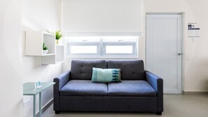 Ein modernes Wohnzimmer mit einem grauen Sofa, einem kleinen Tisch und einem Fenster mit Jalousien.