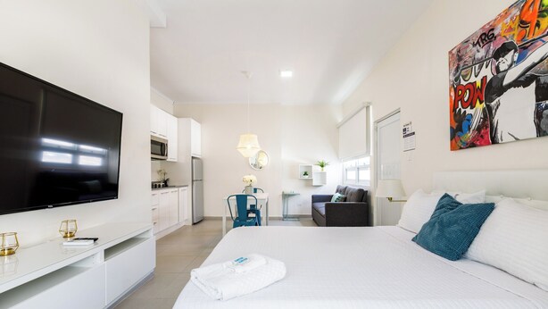 A hotel room with a large bed, a TV, a kitchenette, and a bathroom. - Avila Beach (San Juan)