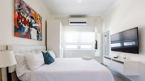 A hotel room with a large bed, a TV mounted on the wall, and a painting above the bed. - Avila Beach (San Juan)