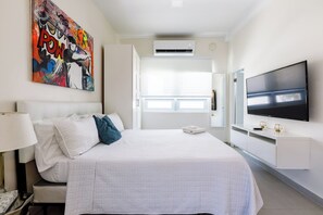 Ein Hotelzimmer mit einem großen Bett, einem an der Wand befestigten Fernseher und einem Gemälde über dem Bett.