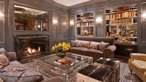 A cozy living room with a fireplace, a sofa, a coffee table, and a bookshelf filled with books and decorative items. - St Regis Residence Club 3 Bedroom - Heart of Downtown Aspen! (Aspen)