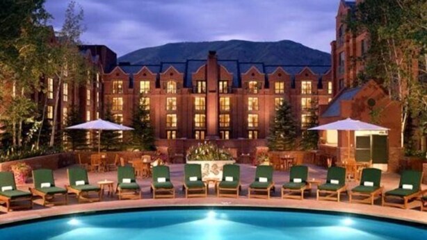 A large building with a swimming pool in front, surrounded by lounge chairs and umbrellas. - St Regis Residence Club 3 Bedroom - Heart of Downtown Aspen! (Aspen)