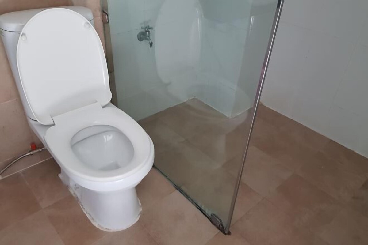 Des toilettes blanches et une douche en verre dans une salle de bain dont le sol est carrelé.