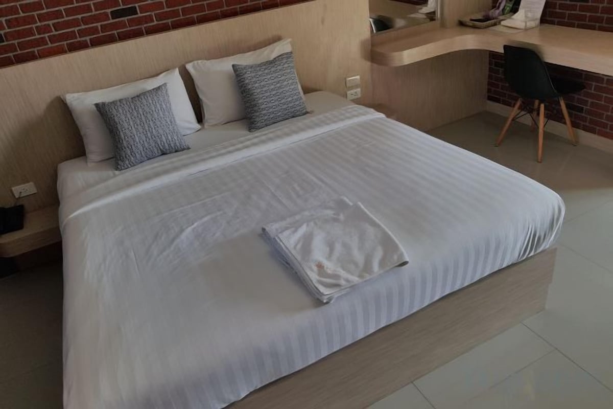 A neatly made bed with a white comforter and pillows, a wooden headboard, and a desk with a chair in a hotel room.