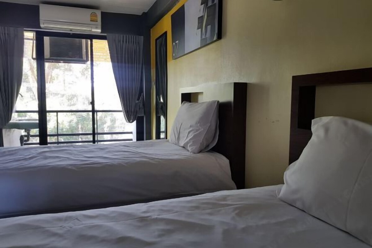 A hotel room with two beds, a window with curtains, an air conditioning unit, and a wall-mounted artwork.