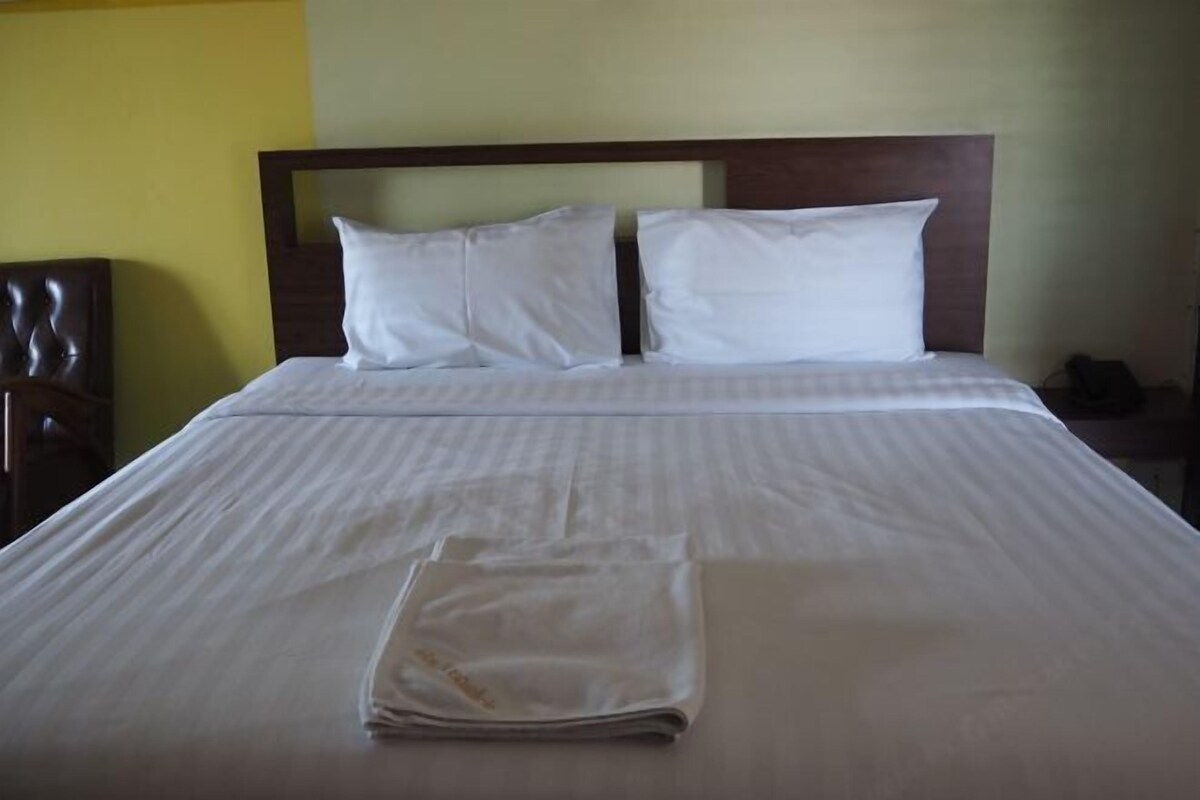 Un lit bien fait, avec des draps et des oreillers blancs, une tête de lit en bois et une couverture pliée posée sur le lit.