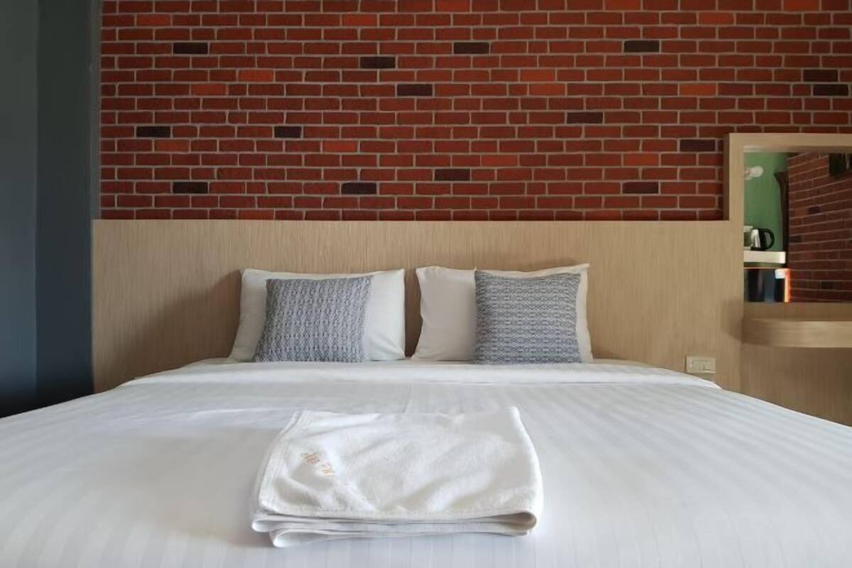 A neatly made bed with a folded white towel, a wooden headboard, and a brick-patterned wall behind it.