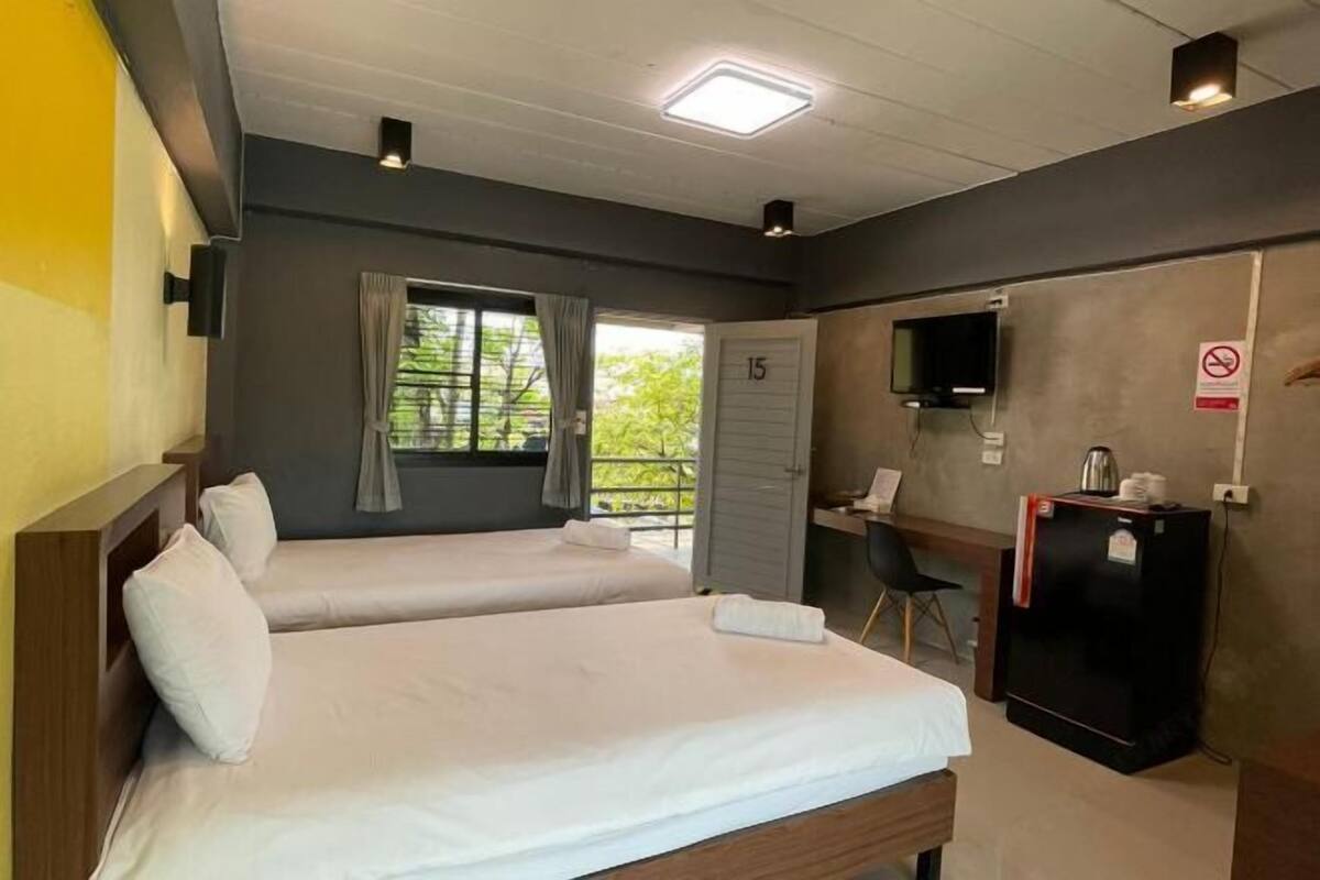 A hotel room with two beds, a desk, a television, a refrigerator, and a window with curtains.