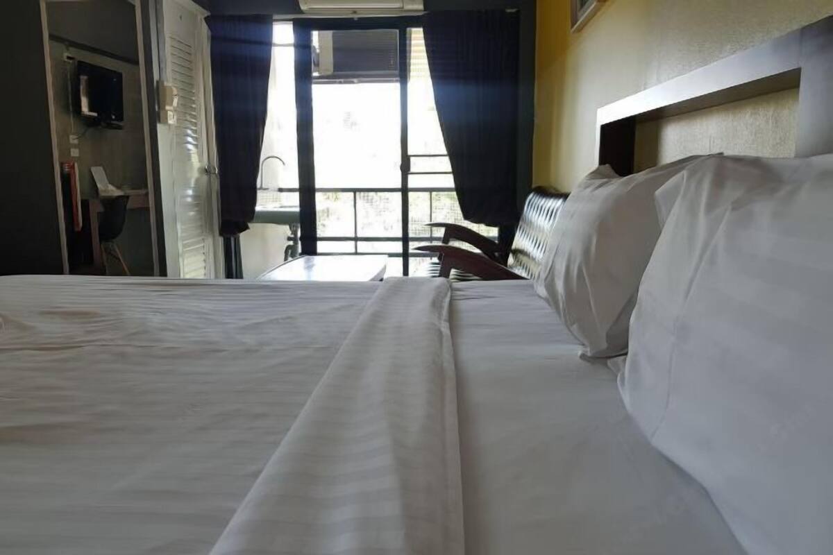 A hotel room with a bed, a chair, a desk, and a window with curtains.