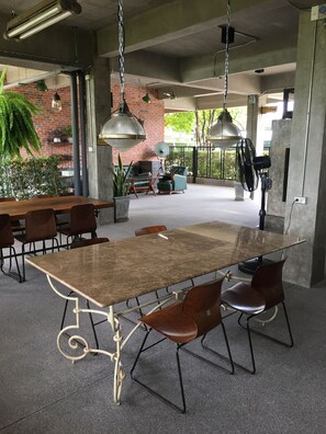 Un espacio interior amplio con una gran mesa de madera rodeada de sillas, pared de ladrillo y lámparas colgantes de estilo industrial.