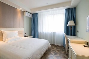 Et hotelværelse med seng, skrivebord, stol og et vindue med gardiner.